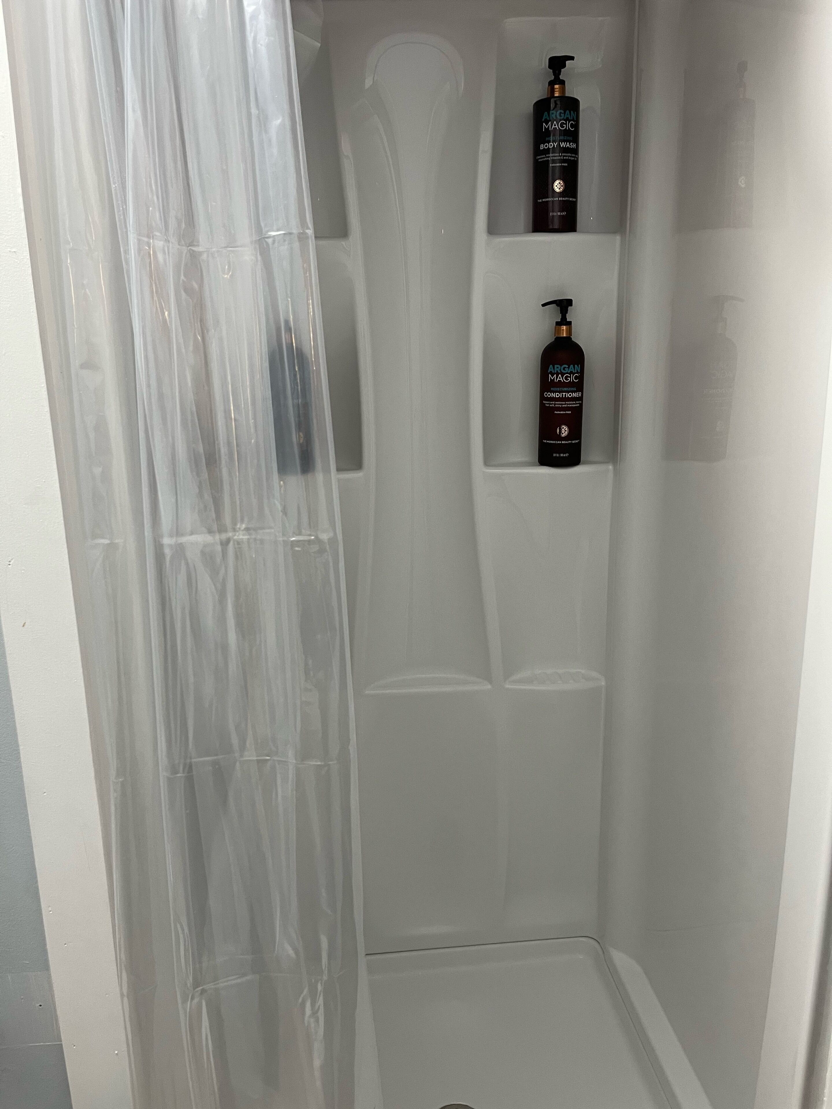 Un baño con cabina de ducha, espejo y dos estantes con botellas de jabón corporal y acondicionador.