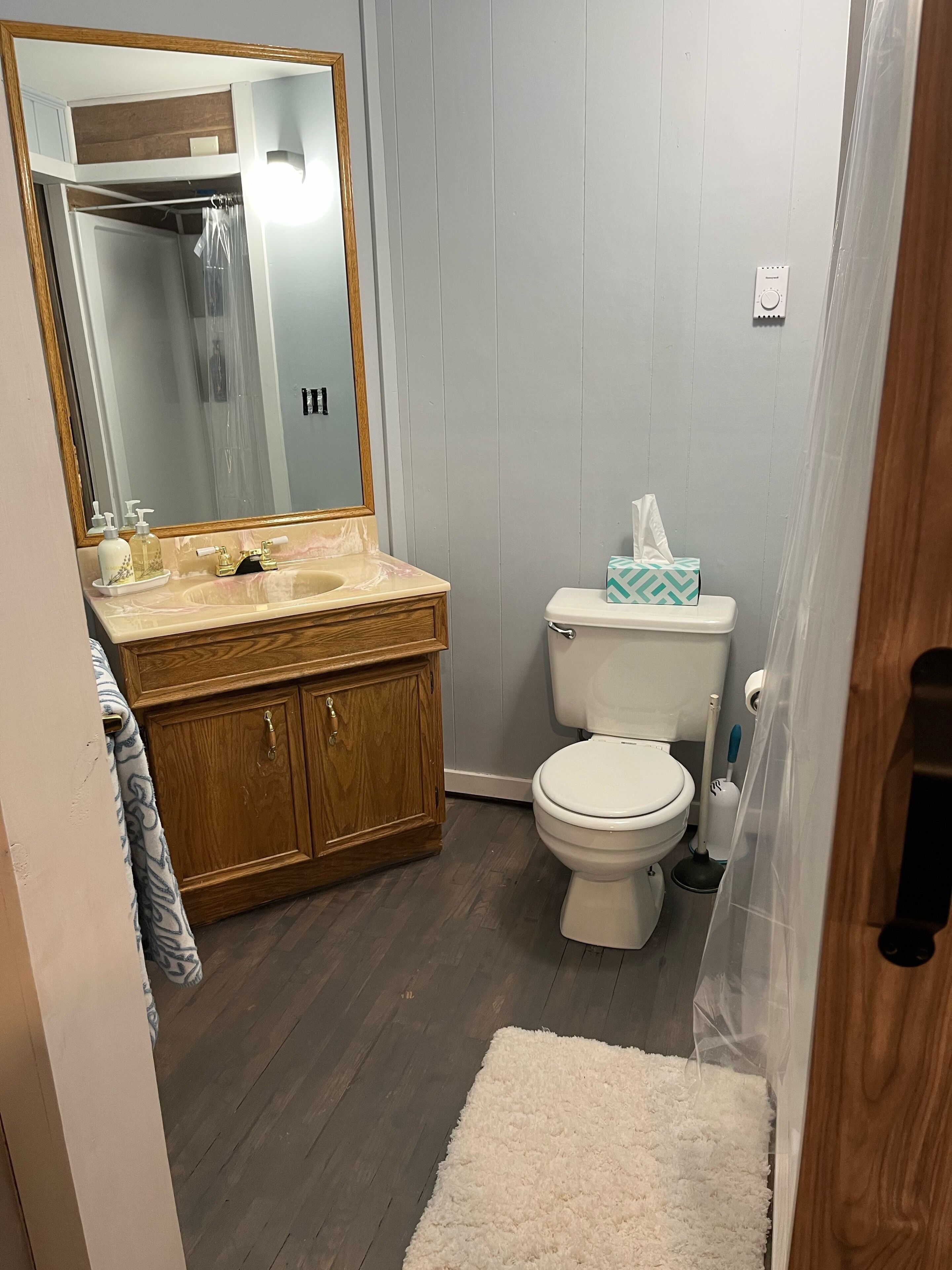 A bathroom with a wooden vanity, a white toilet, a mirror, and a shower curtain.