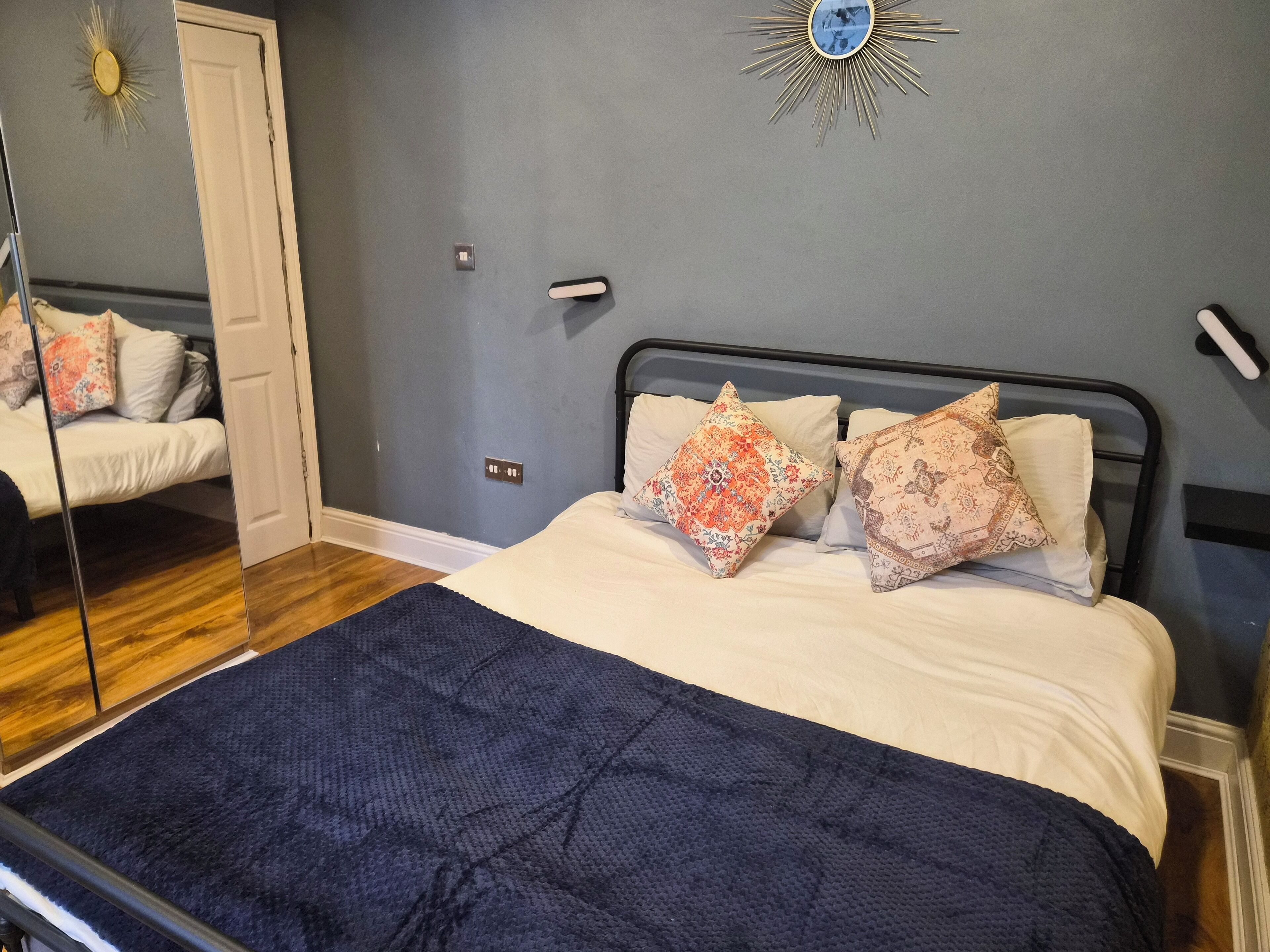 Un dormitorio con una cama, dos almohadones decorativos, un espejo y un reloj de pared.