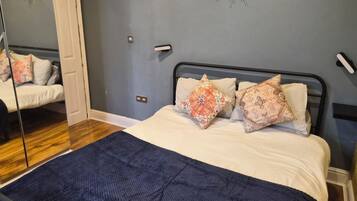 Un dormitorio con una cama, dos almohadones decorativos, un espejo y un reloj de pared.