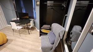 A compact living space with a dining table, chairs, a black sofa, and a small TV. - Dodi Apartments (London)