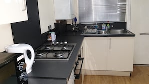 A compact kitchen with a gas stove, a built-in oven, a sink, and a window with blinds. - Dodi Apartments (London)