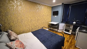 A bedroom with a bed, a desk, and a kitchenette.
