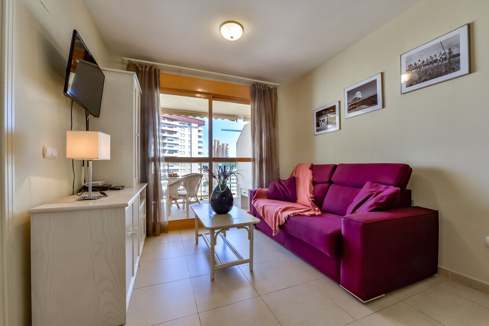 A living room with a sofa, a TV, a table, and a balcony with a chair.