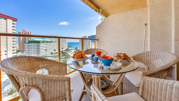 A balcony with wicker chairs, a glass table, and breakfast items. - AMBAR 18B - Apartment with sea views very close to the beach and supermarkets (Calpe)