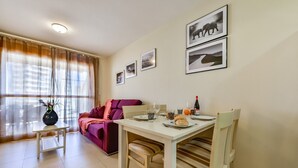 A dining area with a table set for two, a sofa, and a window with curtains. - AMBAR 18B - Apartment with sea views very close to the beach and supermarkets (Calpe)