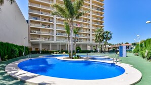 A swimming pool surrounded by a green deck, with a multi-story building in the background. - AMBAR 18B - Apartment with sea views very close to the beach and supermarkets (Calpe)
