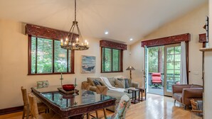 Un salón espacioso con una mesa de comedor de madera, asientos cómodos y ventanas grandes con contraventanas.
