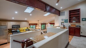 Una cocina amplia con una isla central, vigas de madera en el techo y vistas al área de estar.