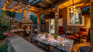 Un patio al aire libre con suelo de piedra, una chimenea de piedra y una mesa de comedor para seis personas, con velas y platos.