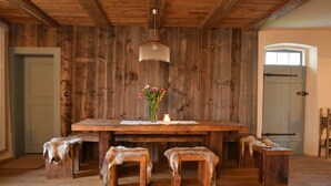 Ein rustikaler Essbereich aus Holz mit einem großen Tisch, Bänken und einer hängenden Leuchte.
