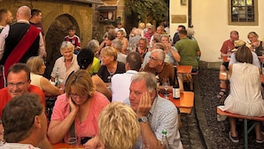Ein belebter Außenbereich mit Gastronomie, traditionellen Fachwerkhäusern und Steinmauern.