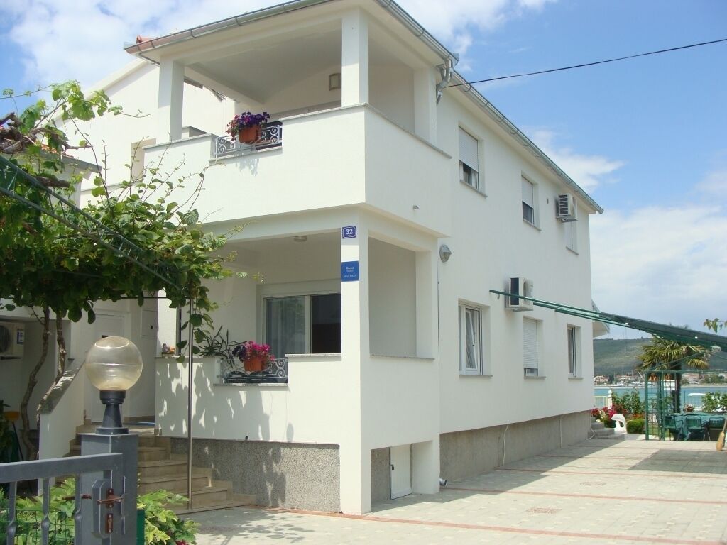 Un bâtiment à deux étages doté d’un balcon, d’une enseigne indiquant le numéro de chambre 32, et d’un petit espace extérieur aménagé avec des tables et des chaises.