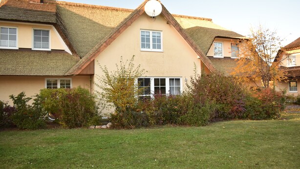 A traditional house with a thatched roof, a central chimney, and a small garden with various shrubs and a lawn. - Holiday apartments in the middle of the biosphere reserve (Middelhagen)