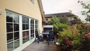 A patio with a table and chairs, a sliding glass door, and a garden with bushes and flowers. - Holiday apartments in the middle of the biosphere reserve (Middelhagen)