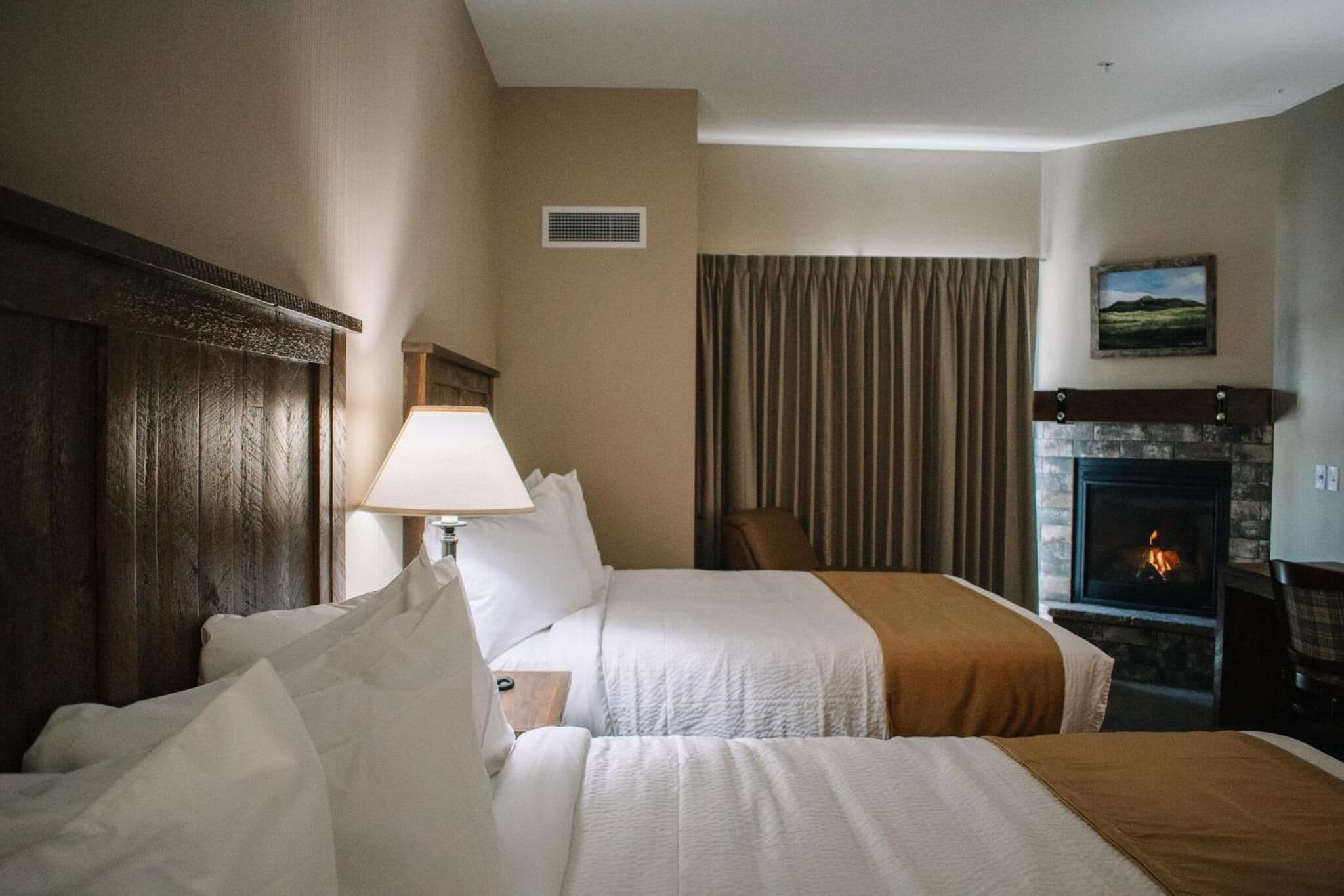 Een hotelkamer met twee bedden, een openhaard, een lamp en een schilderij aan de muur.