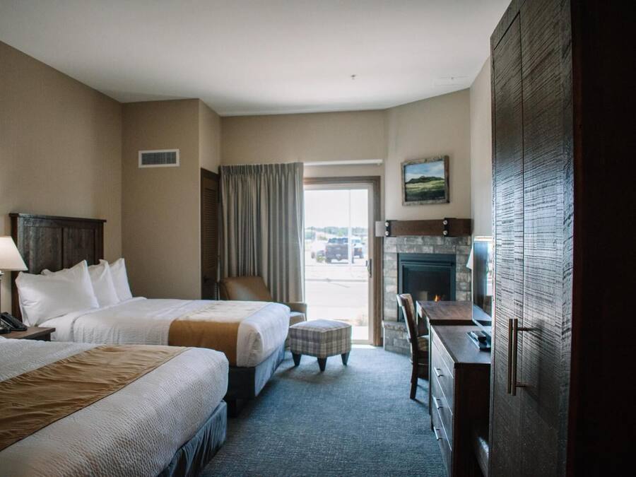 Habitación de hotel con dos camas, un escritorio, una silla, una chimenea y vista al estacionamiento.