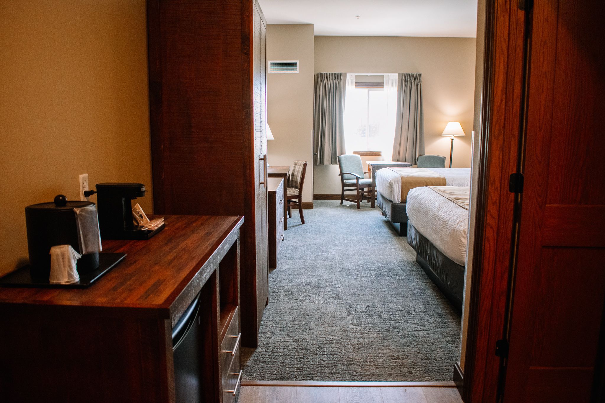 Et hotelværelse med en seng, et skrivebord, en stol og et lille bord med en lampe.