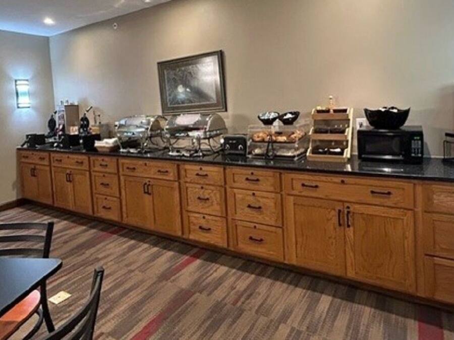 A kitchen with wooden cabinets, a black countertop, a clock, and various appliances.