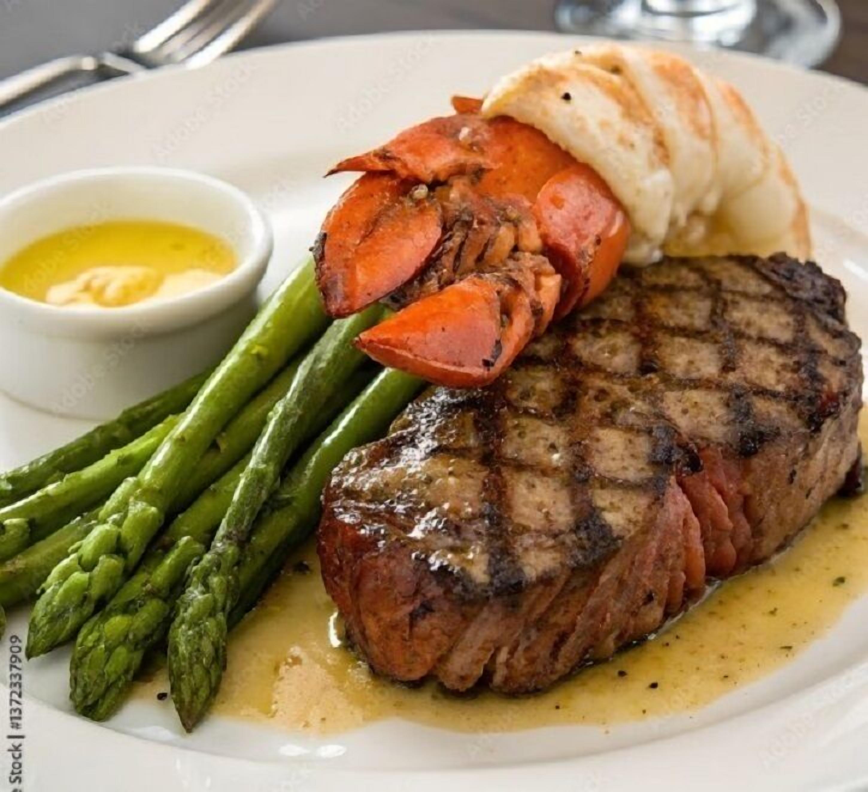 Een bord met gegrilde steak, asperges en een kreeftstaart.