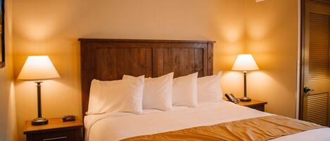 A neatly made bed with white linens, two bedside lamps, a wooden headboard, and a brown throw blanket.