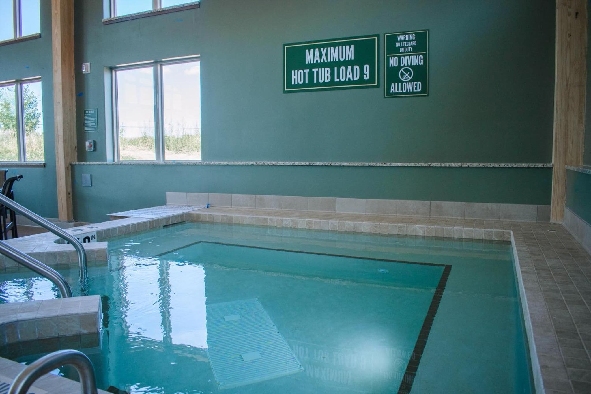 Una piscina interior con señalización de seguridad clara, incluyendo una advertencia sobre la capacidad máxima del jacuzzi y prohibición de clavados.