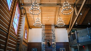 Un vestíbulo de hotel con vigas de madera, candelabros, una pared de piedra y una cabeza de alce montada.