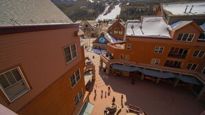 Ein Skigebiet mit einem zentralen Innenhof, Gebäuden mit Holzfassaden und einem schneebedeckten Berg im Hintergrund.
