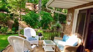 A covered outdoor deck with wicker furniture, including a rocking chair, a sofa, and a small table. - Walk to private beach in Clearwater (East Hampton)