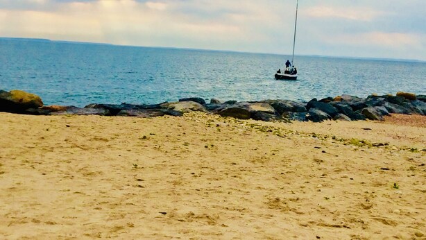 A sandy beach with a rocky shoreline and a sailboat in the distance. - Walk to private beach in Clearwater (East Hampton)