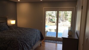 A bedroom with a bed, a nightstand, a lamp, a sliding glass door leading to an outdoor area with a pool. - Walk to private beach in Clearwater (East Hampton)
