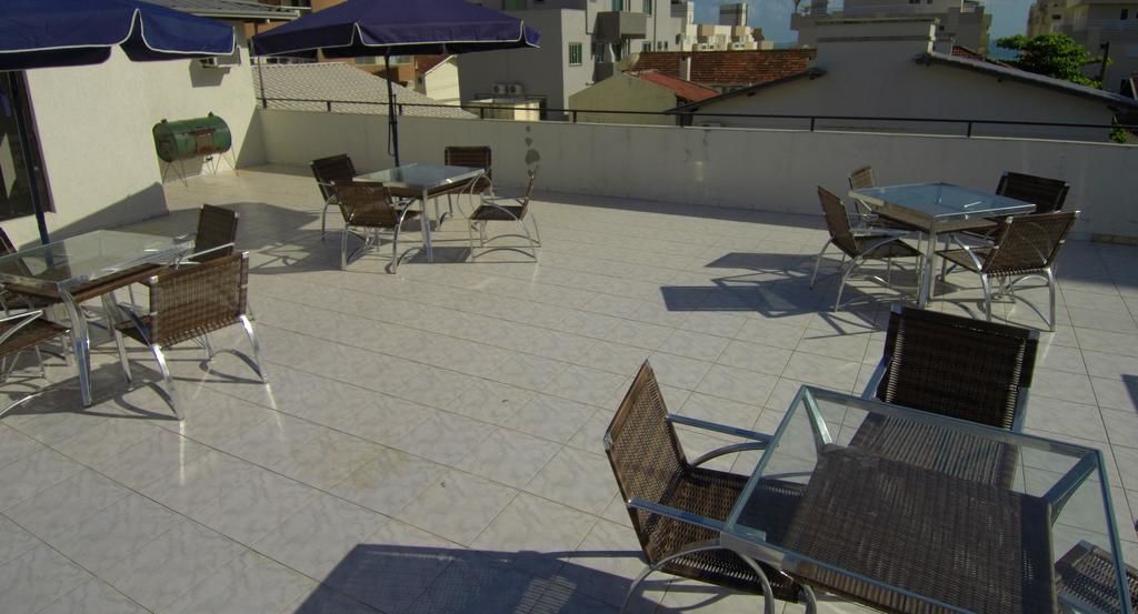Terraza en la azotea con mesas de vidrio y sillas de mimbre, rodeada de sombrillas azules.