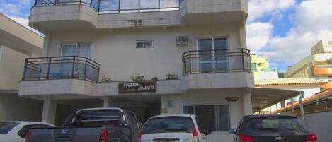 A multi-story building with a sign reading "POUSADA ÁGUA VIVA." There are three cars parked in front, and the building has balconies with glass railings.