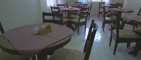 Un comedor con varias mesas y sillas, algunas con manteles rosas.