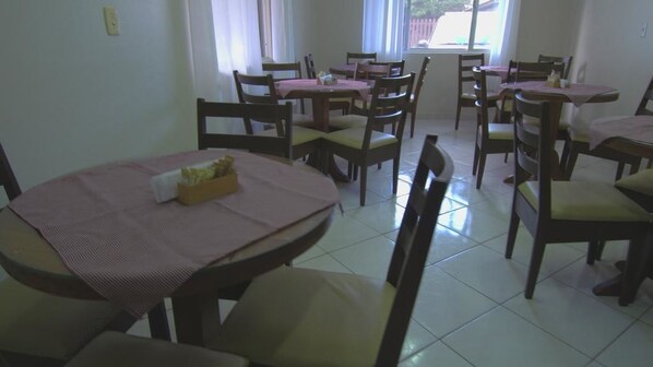 Un comedor con varias mesas y sillas, algunas con manteles rosas.