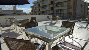 Un patio al aire libre con una mesa de vidrio y sillas de mimbre, rodeado por un edificio de gran altura.