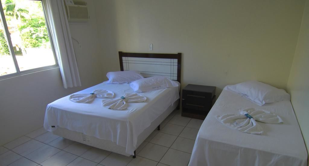A hotel room with two beds, each with white linens and towels arranged in a bow shape. There is a small bedside table between the beds.