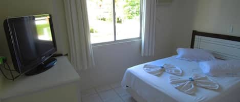 A hotel room with a bed, a TV on a white table, and a window with curtains.