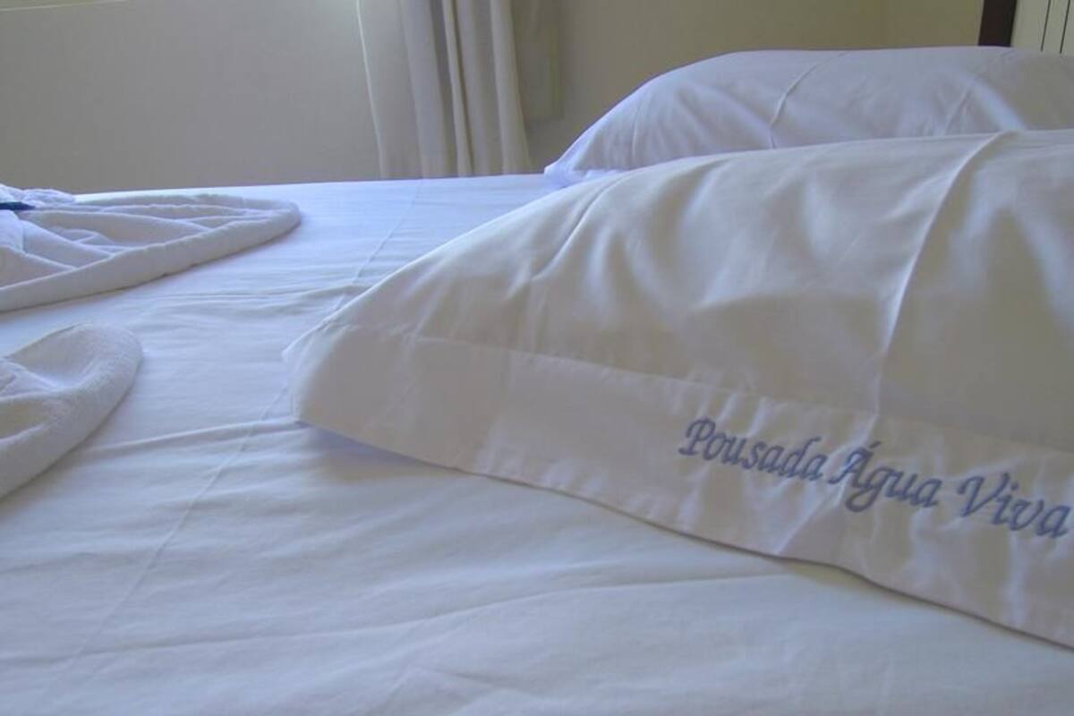 Cama com roupa de cama branca e travesseiro com bordado.