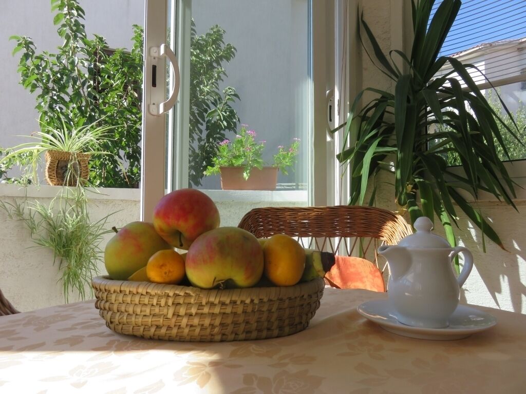 A table with a basket of fruits and a teapot on a tablecloth.
