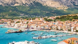 A coastal town with a marina filled with boats, surrounded by colorful buildings and green hills in the background. - Apartment in Baška with Terrace, Air condition, WIFI (883-2) (Baška)