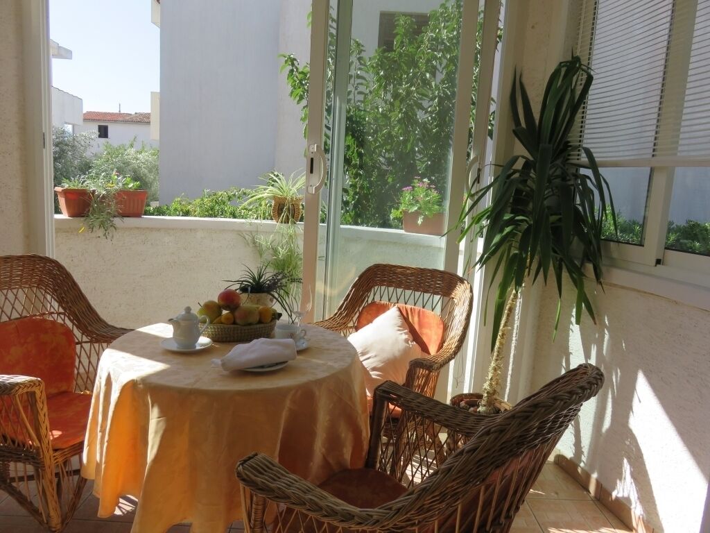 Eine sonnendurchflutete Terrasse mit Korbmöbeln, einem runden Tisch mit Obstschale und Topfpflanzen.