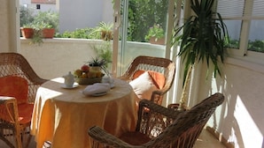 A sunlit patio with wicker furniture, a round table with a fruit bowl, and potted plants. - Apartment in Baška with Terrace, Air condition, WIFI (883-2) (Baška)