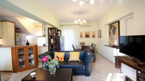 A living room with a sofa, coffee table, and a TV. There is a kitchen area with a refrigerator and a dining table with chairs. - Villa Sonia (Anthemis villas) - Private Pool, private BBQ, playground for kids! (Kariotes)