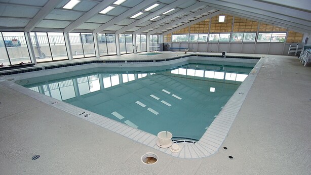 Una piscina interior con señalización clara, un trampolín y una estructura de techo cubierta.