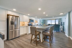 A modern kitchen with a stainless steel refrigerator, a microwave, and a large island with bar stools.