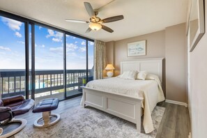 Una camera da letto con una grande finestra, un ventilatore a soffitto, un letto, un comodino e una sedia.
