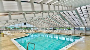 Una piscina interior con agua cristalina y azul, rodeada de sillones blancos y un techo de vidrio.