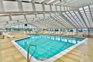Una piscina interna con acqua cristallina e blu, circondata da comode poltrone bianche e un soffitto in vetro.