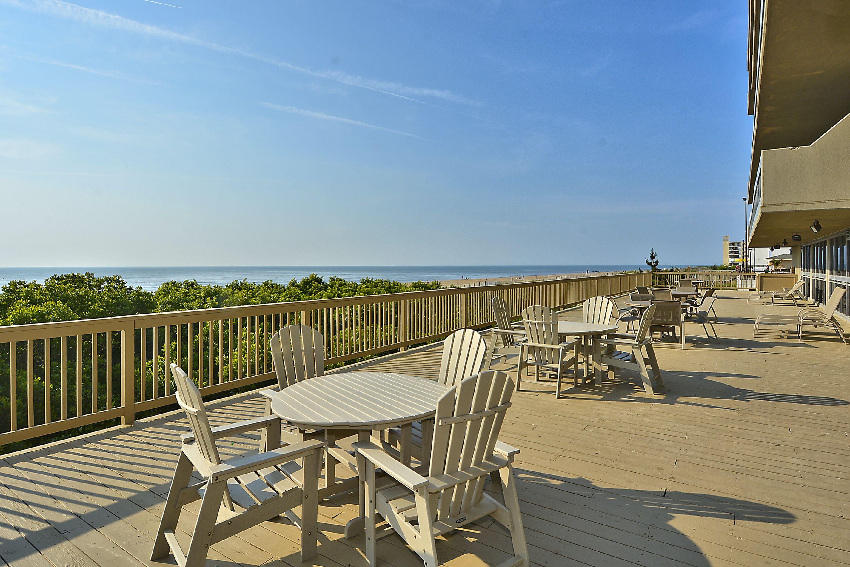 A wooden deck with tables and chairs, overlooking a beach.